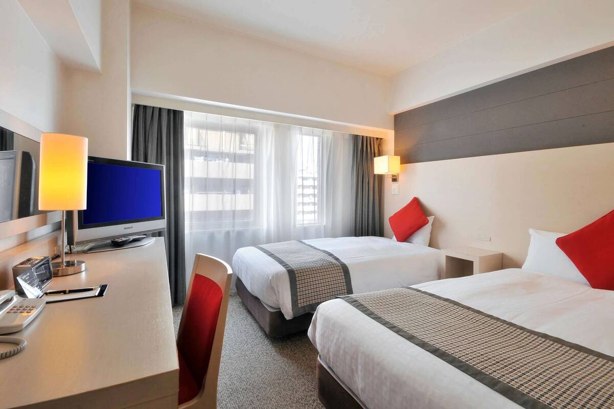 A hotel room with two beds, a desk with a computer, a telephone, and a lamp.