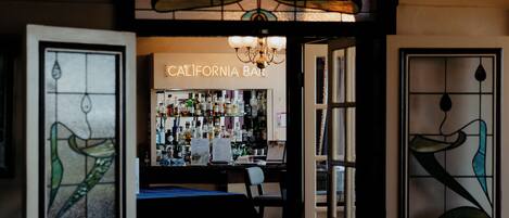 A bar area with a sign reading "CALIFORNIA BAR," a chandelier, and a glass partition with a bird design.