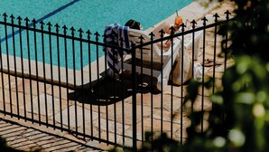 Une piscine entourée d’une clôture en métal, une chaise longue et une serviette.