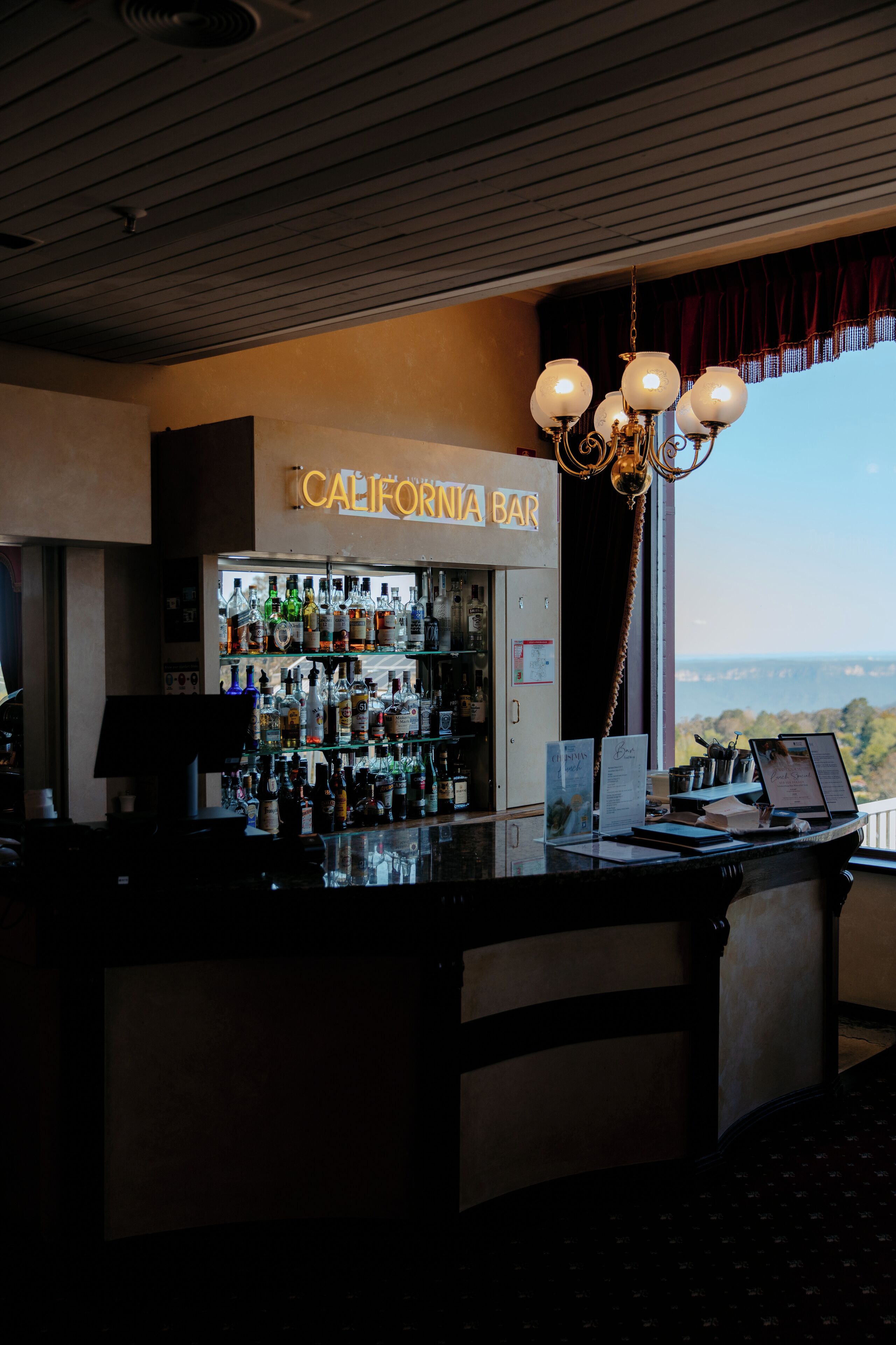 Eine Bar mit Blick auf die Landschaft, ein Neon-Schild mit der Aufschrift "California Bar" und eine Auswahl an Flaschen in Regalen.