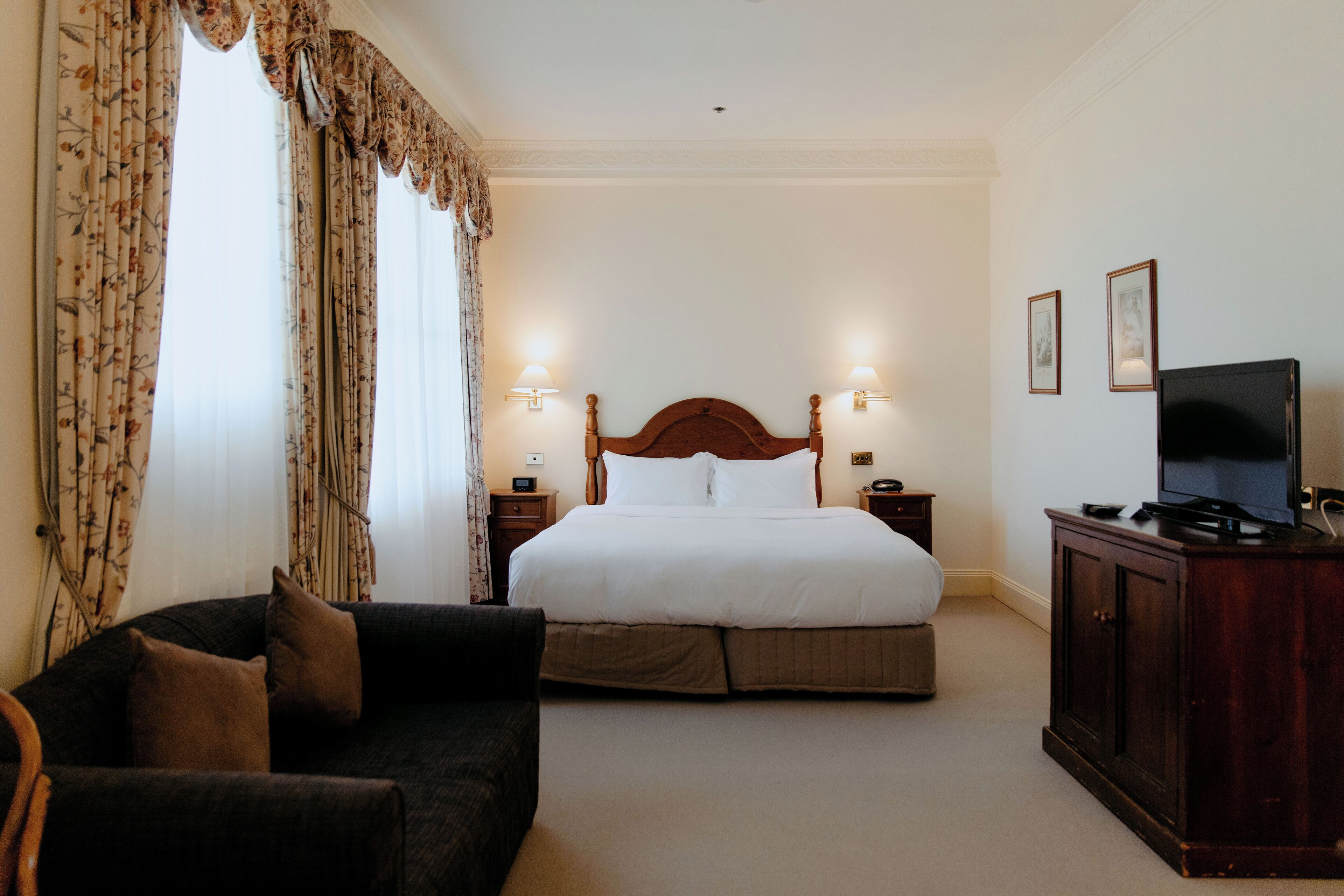 A hotel room with a bed, a dark-colored sofa, a TV, and two bedside lamps.