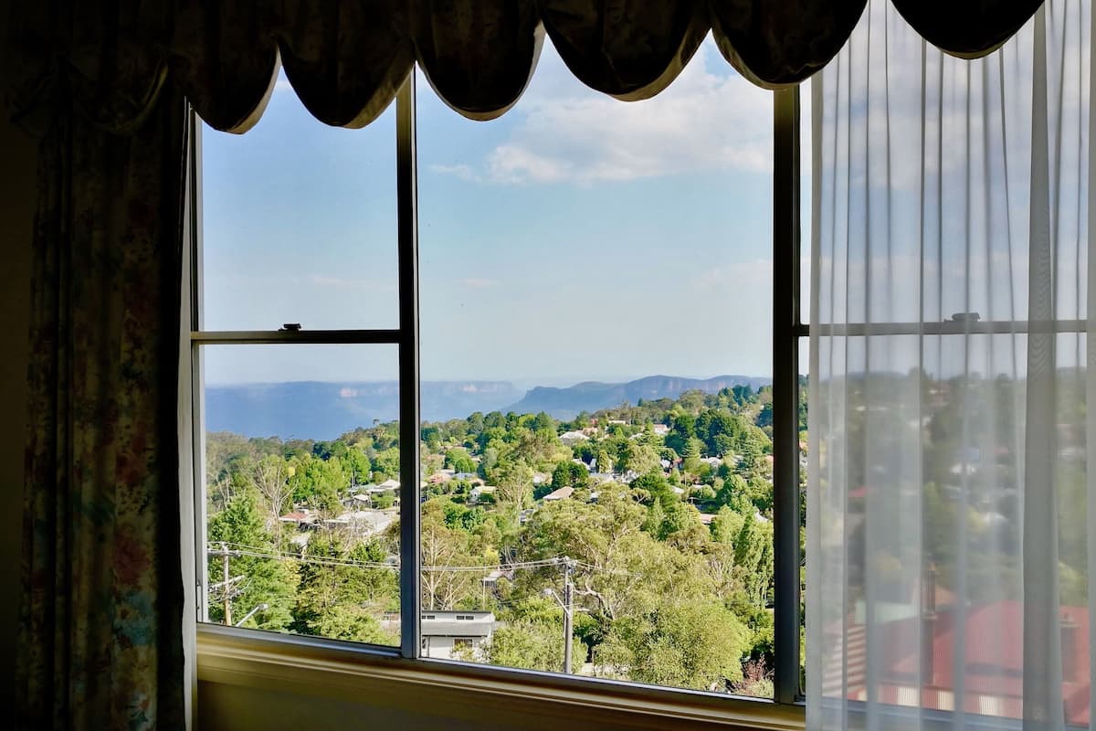 A room with a large window offering a view of a residential area with trees and houses.