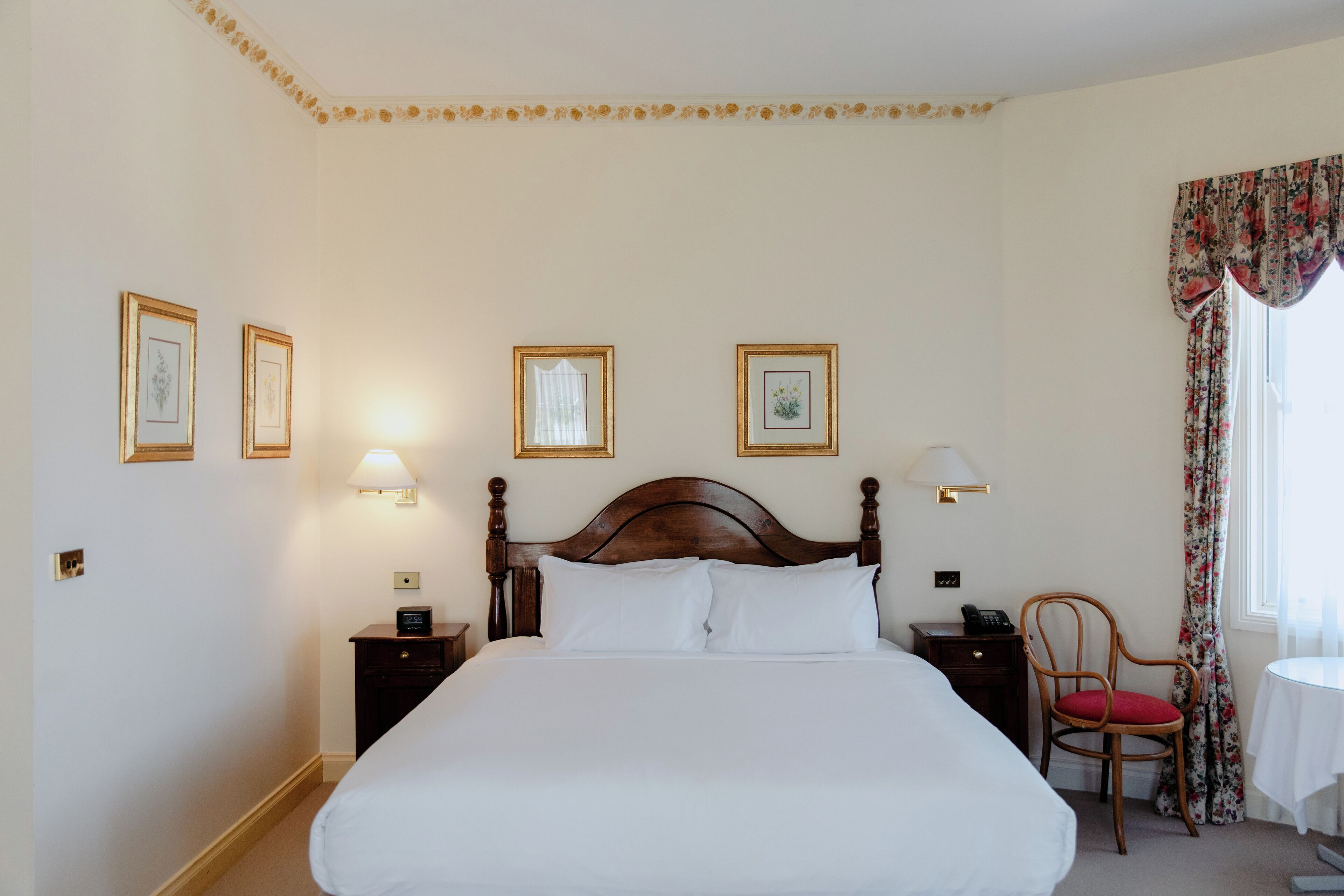 Habitación de hotel ordenada con una cama grande, mesitas de noche, una silla y una pequeña mesa.