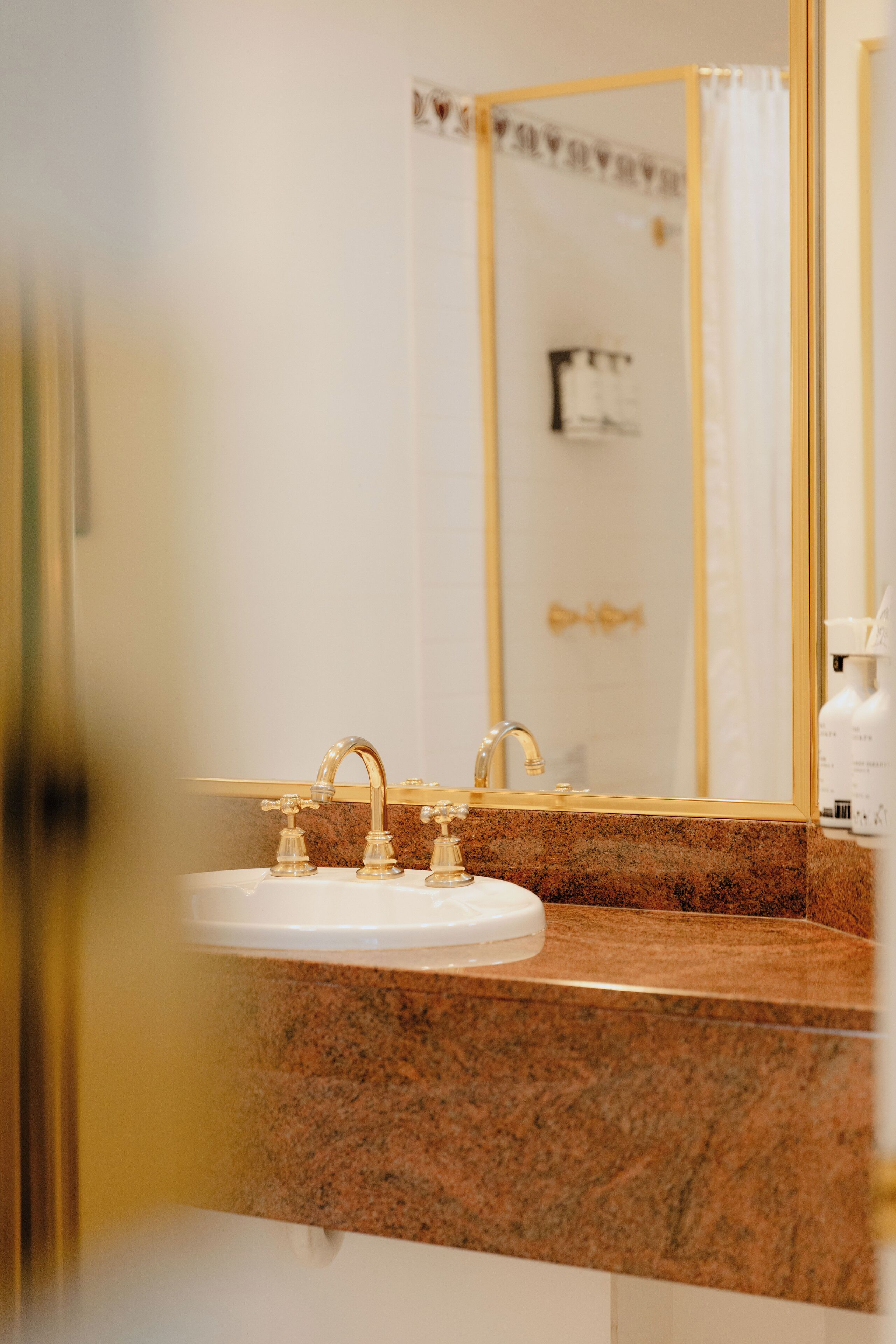 A bathroom with a granite countertop, gold faucets, and a mirror with a gold frame.
