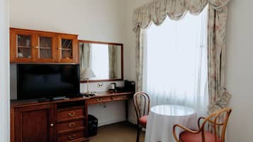 Habitación de hotel con escritorio de madera, televisor de pantalla plana, espejo, pequeña mesa con mantel blanco y dos sillas de mimbre.
