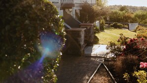 Una casa de dos pisos con un balcón, un jardín con flores y un cielo despejado.