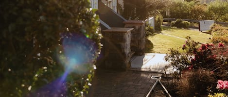 Una casa de dos pisos con un balcón, un jardín con flores y un cielo despejado.