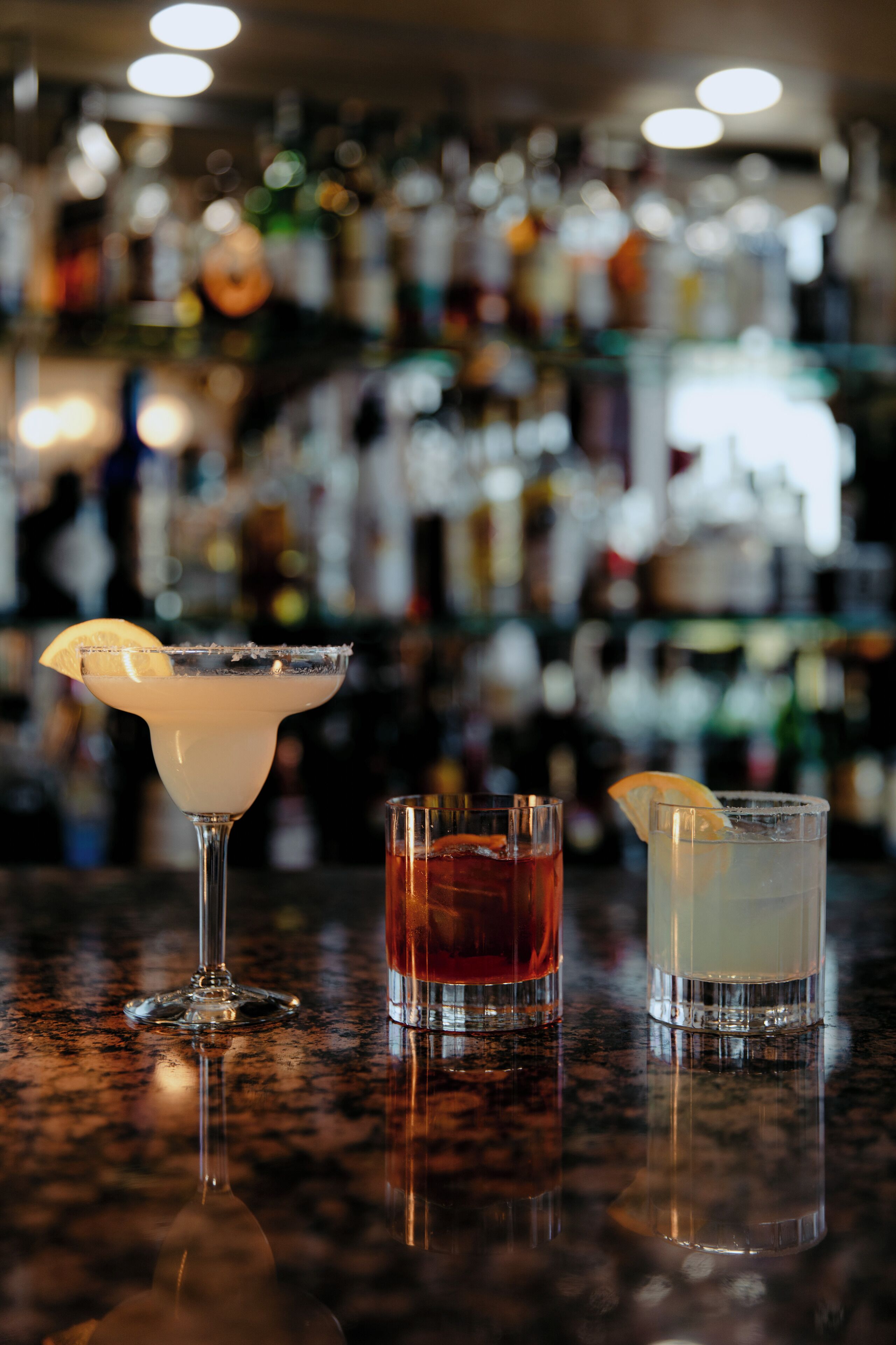 Three drinks on a bar counter with a blurred background of bottles.
