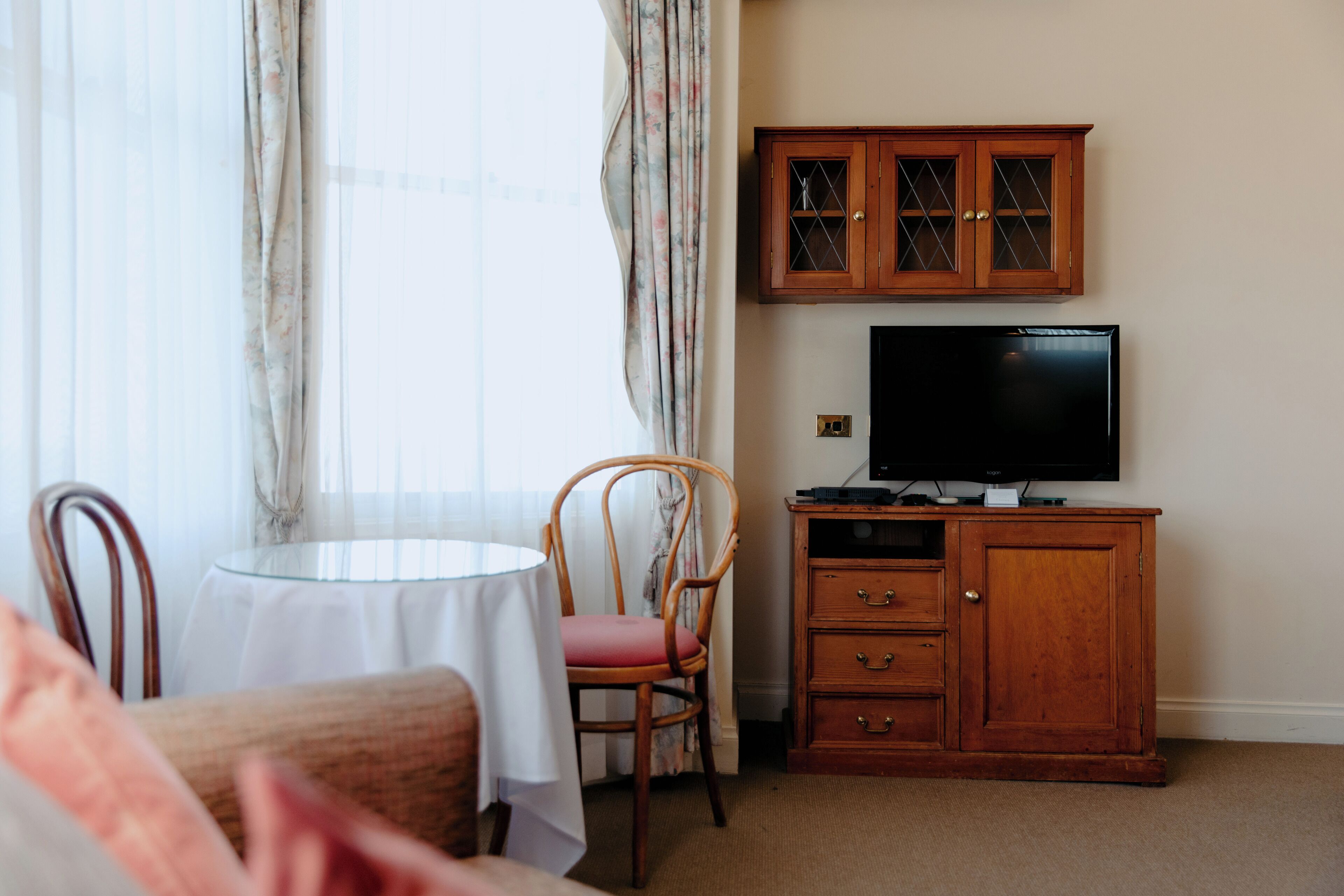 Een hotelkamer met een eettafel, een stoel, een televisie en een houten kast.