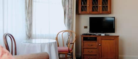 Een hotelkamer met een eettafel, een stoel, een televisie en een houten kast.