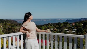 Una persona en un balcón con vistas a un paisaje pintoresco con colinas y casas.