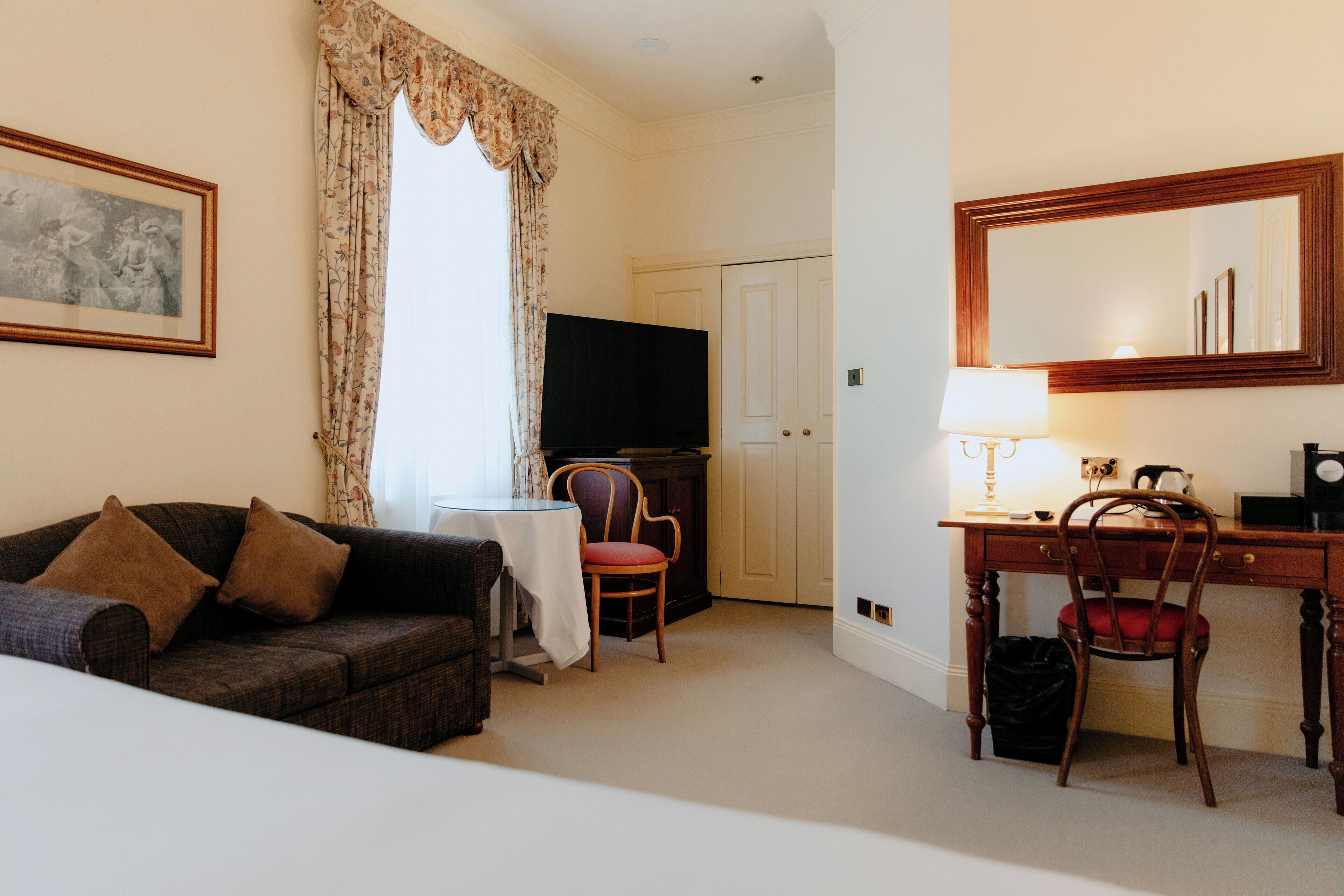 Une chambre d’hôtel comprenant un canapé, une table à manger, une chaise, un bureau avec une chaise, une télévision, une lampe et un miroir.