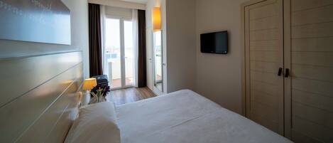 A hotel room with a bed, a TV mounted on the wall, a wardrobe, and a view of the outdoors through a door.