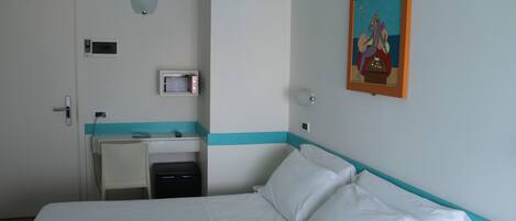 A hotel room with a bed, a desk, a chair, a small table, and a painting on the wall.