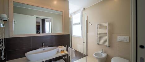 A modern bathroom with a large mirror, a white sink, a bidet, and a toilet.