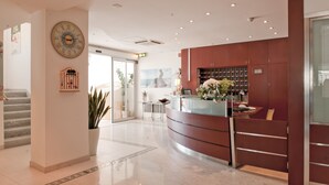Un moderno vestíbulo de hotel con mostrador de recepción, un gran reloj de pared y una escalera que sube a otro piso.