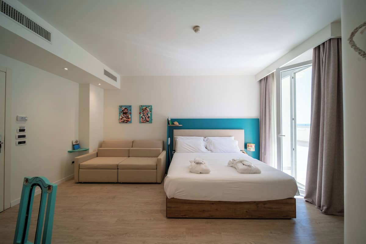 A modern hotel room with a large bed, a sofa, and a view of the outdoors.