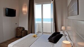 Una habitación de hotel con cama, televisión, maleta y vista al océano.