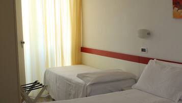 A hotel room with two single beds, a red accent wall, a window with curtains, and a wall-mounted light.