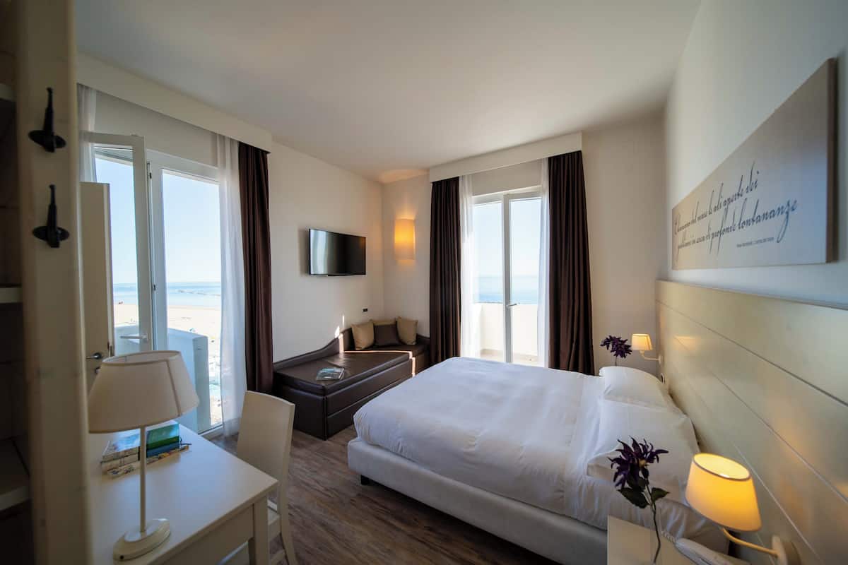A hotel room with a bed, a desk, a chair, a TV, and a window with curtains.