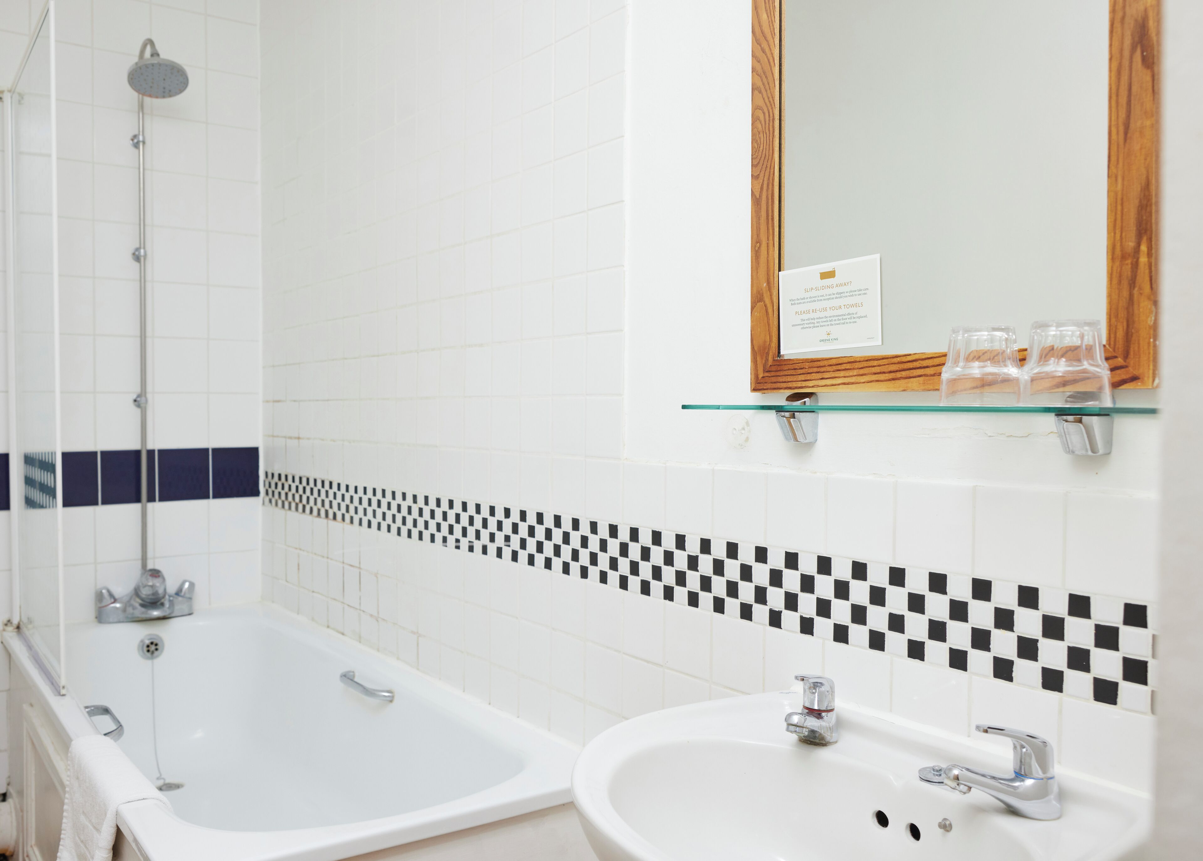 A bathroom with a bathtub, a sink, a mirror, and a glass shelf with toiletries.
