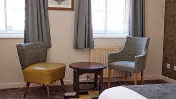 A hotel room with a bed, a small round table, two chairs, a radiator, and a framed picture on the wall.