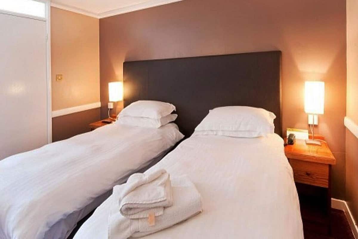 Una habitación de hotel con dos camas individuales, cada una con mesita de noche y lámpara.