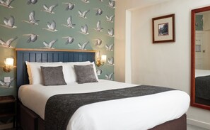 A hotel room with a bed, a nightstand, a wall-mounted light fixture, and a framed picture on the wall.