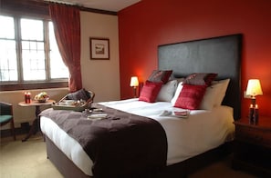 A hotel room with a large bed, two bedside lamps, a small table with a tray of breakfast, and a chair.