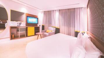 A hotel room with a large bed, a desk with a TV, a chair, and a small table.