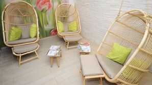 Een kamer met rieten stoelen en een bank, elk met groene kussens, en kleine tafeltjes met tijdschriften.