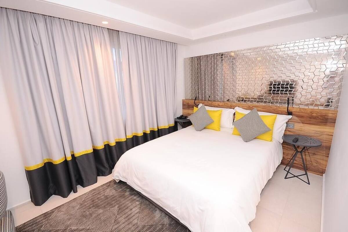 Une chambre d’hôtel moderne avec un grand lit, une tête de lit en bois et un mur orné d’un motif géométrique.