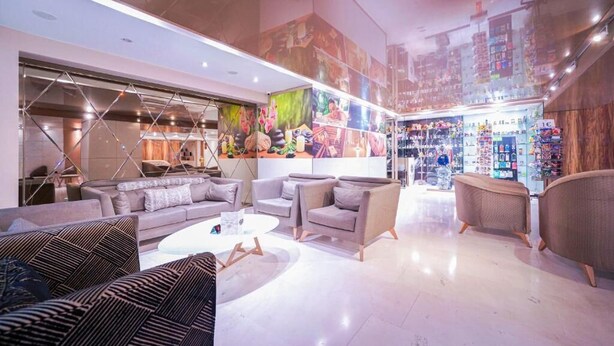 Een moderne hotellobby met een zithoek, een groot muurschildering en een zichtbare winkel met diverse artikelen.