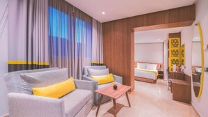 Een hotelkamer met een bank, fauteuil en een klein tafeltje. Er staat een bed met een wit hoofdeinde en een gele accentkleur. De kamer heeft houten lambrisering en een grote spiegel aan de muur.