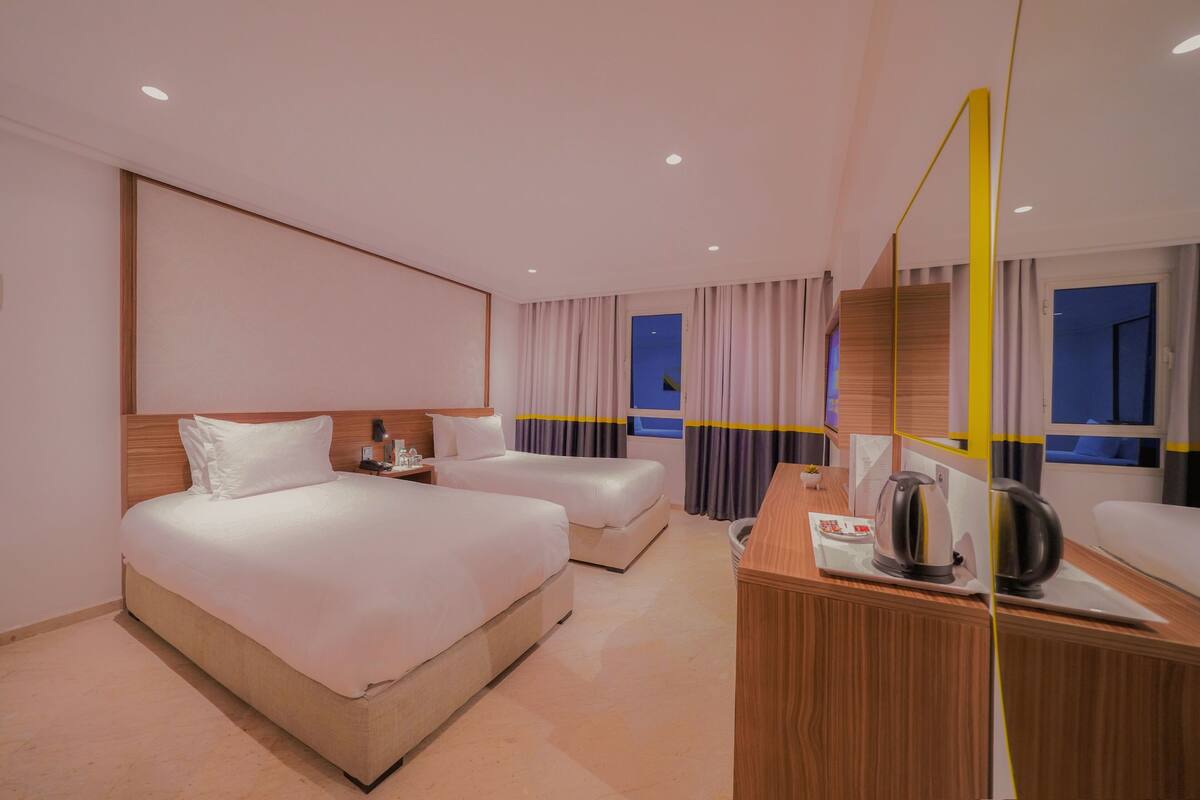 Une chambre d’hôtel avec deux lits, un bureau en bois, un miroir et une vue sur le ciel nocturne.