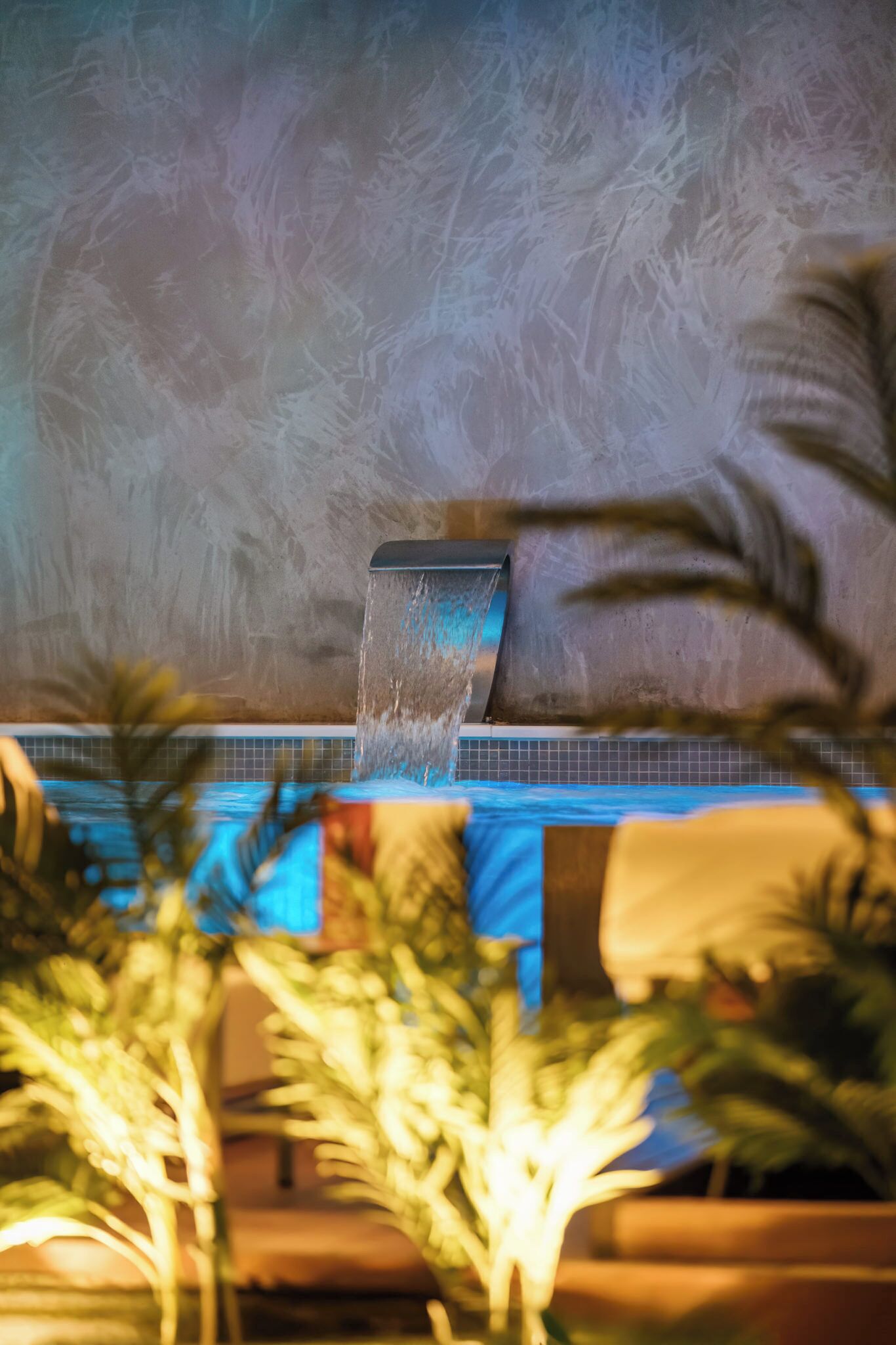 Ein Wasserspiel mit Wasserfall, einem mit Fliesen ausgekleideten Pool und Palmen.