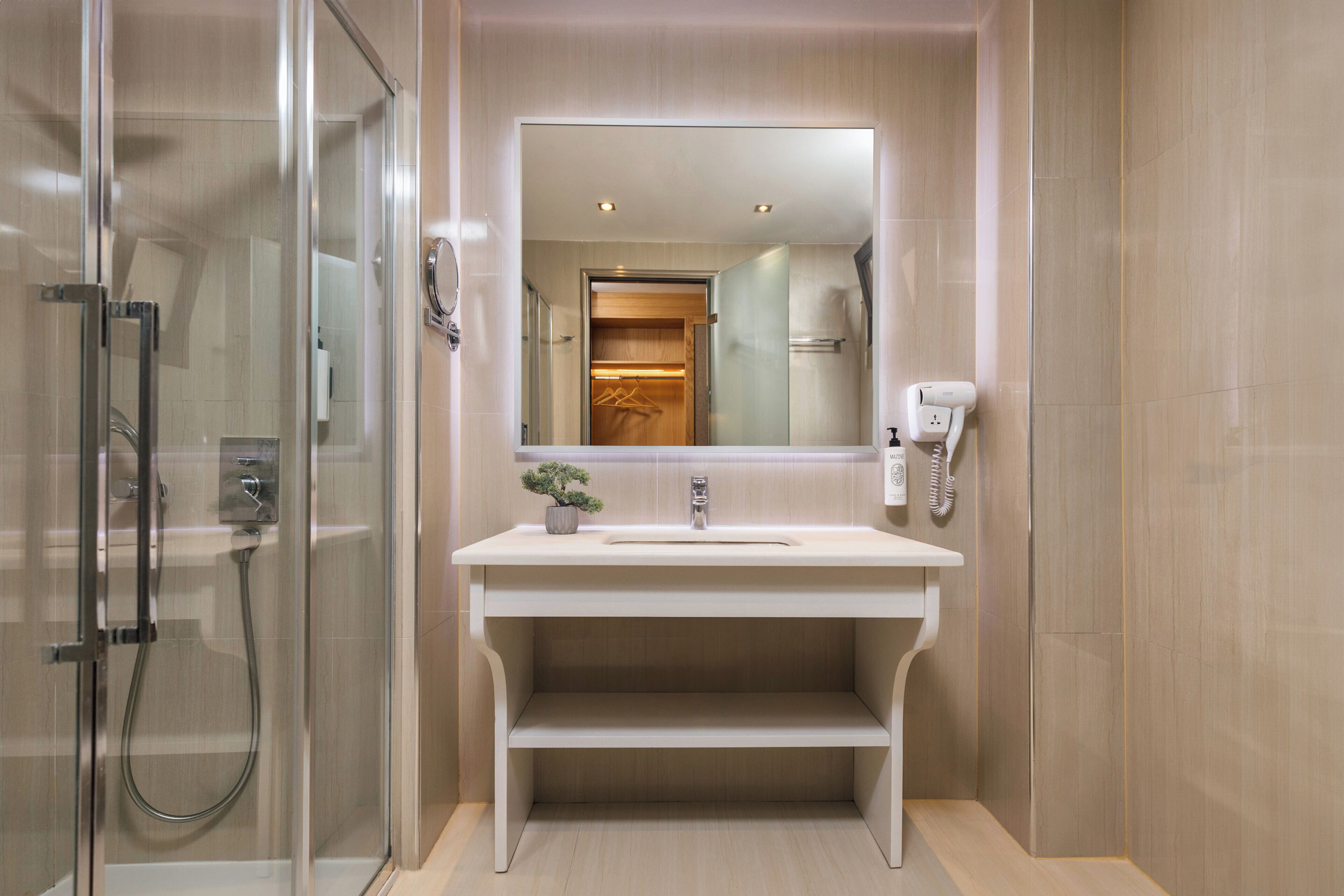 A modern bathroom with a glass-enclosed shower, a white sink with a mirror above it, and a wooden door leading to another room.