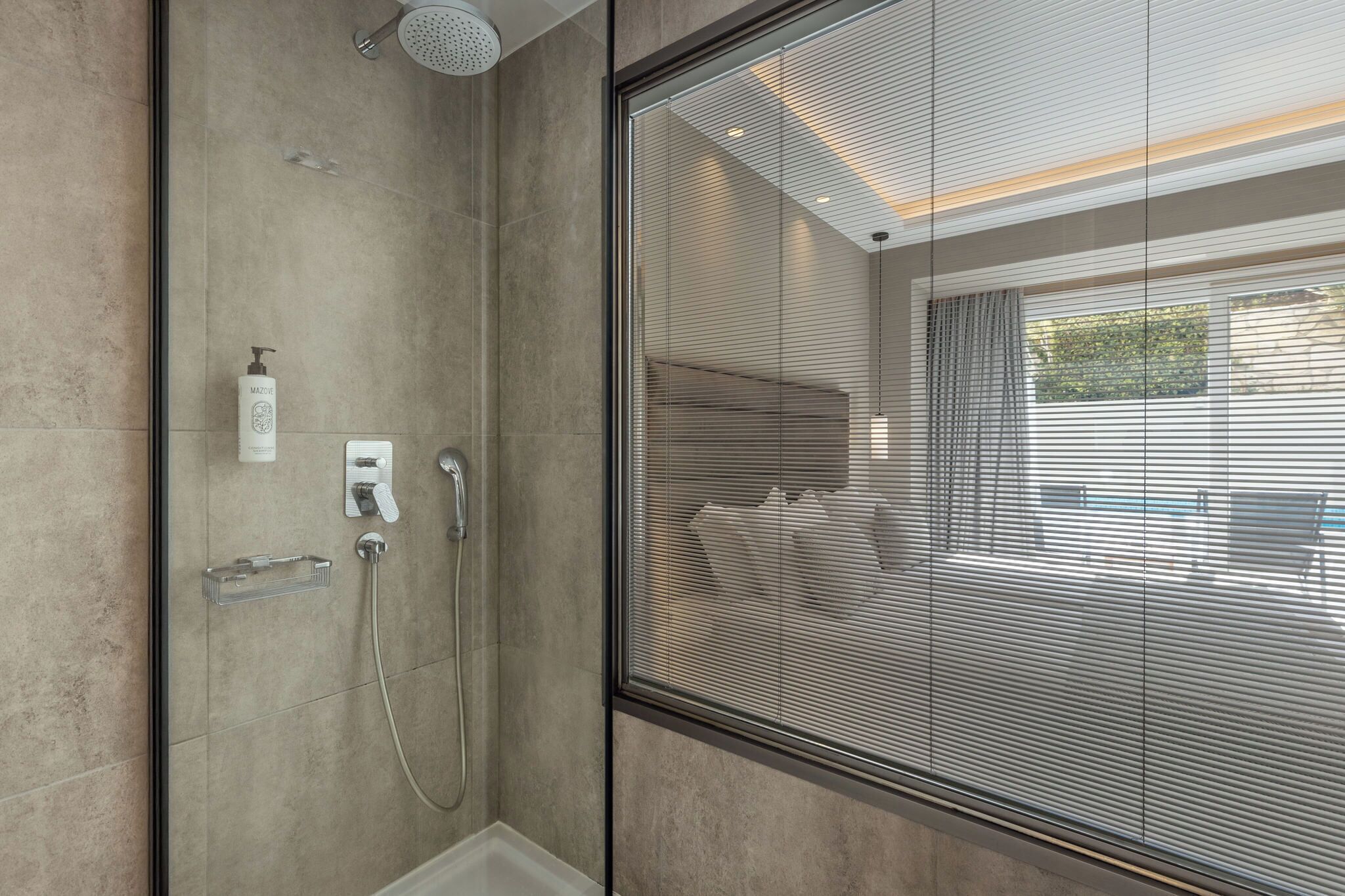 A modern bathroom with a glass shower enclosure, a handheld showerhead, and a handheld soap dispenser.