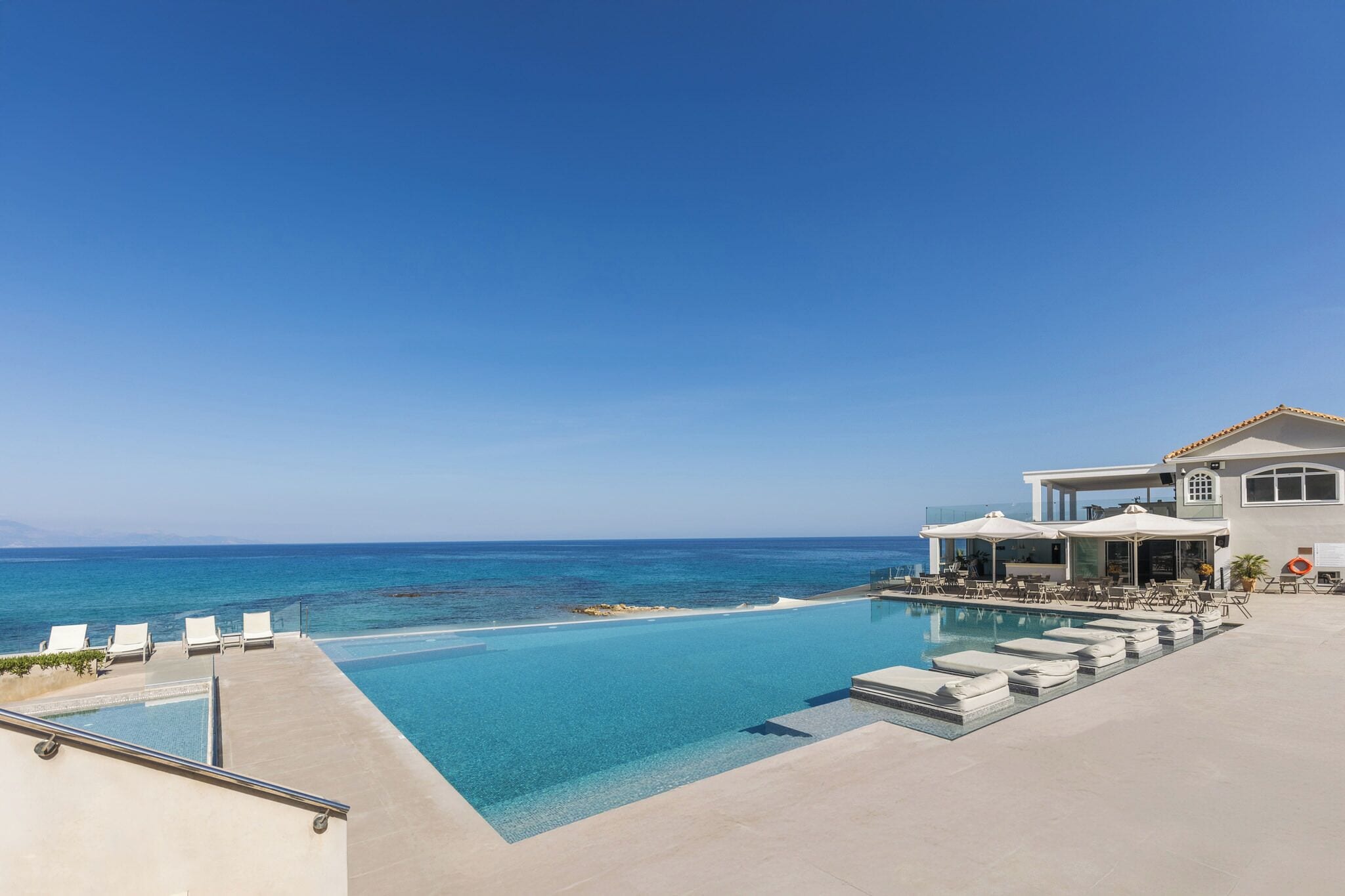 Una piscina di resort con acqua cristallina, sedie a sdraio bianche e vista sull'oceano.