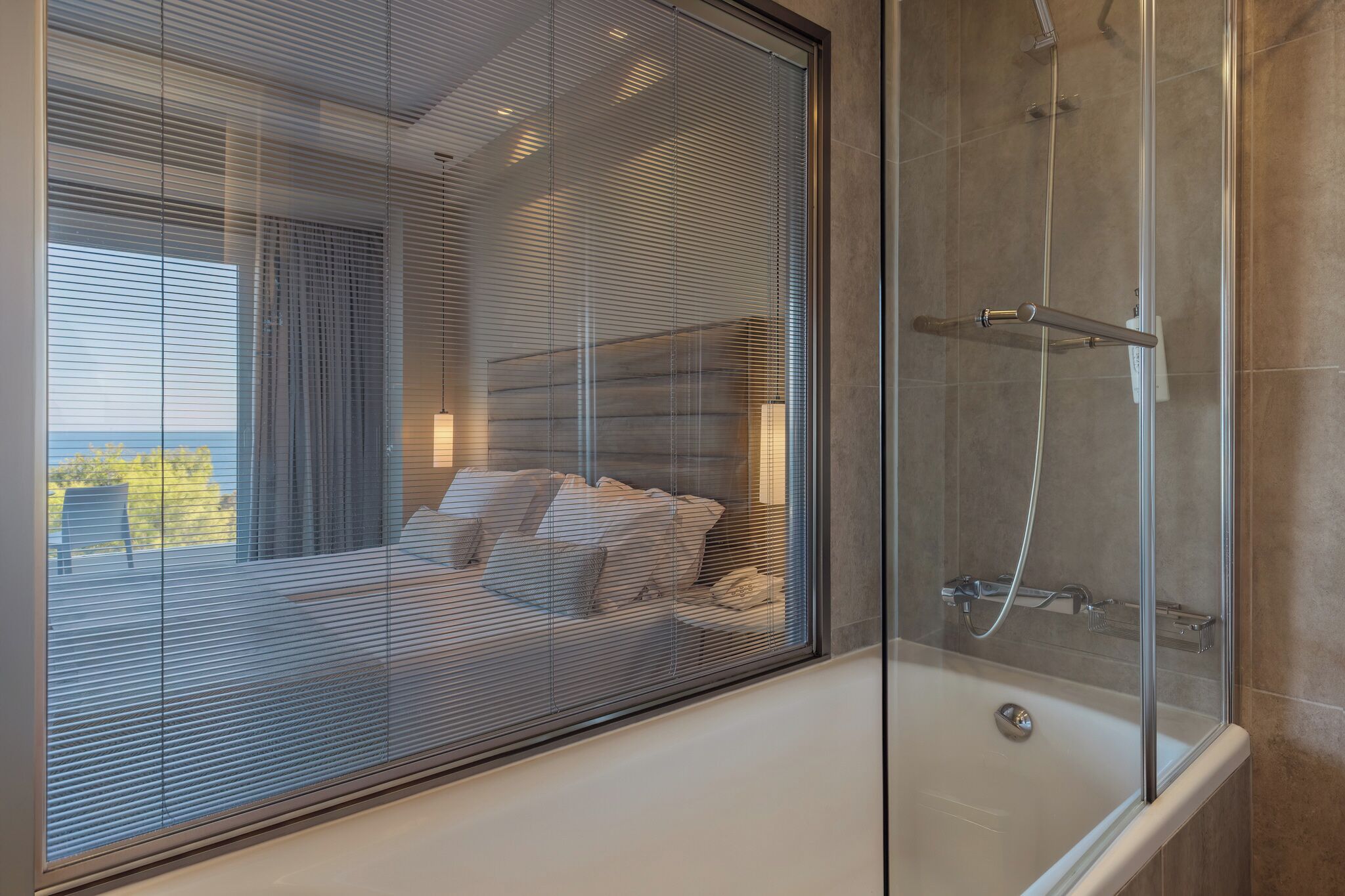 A modern bathroom with a glass shower enclosure, a bathtub, and a view through a large window.