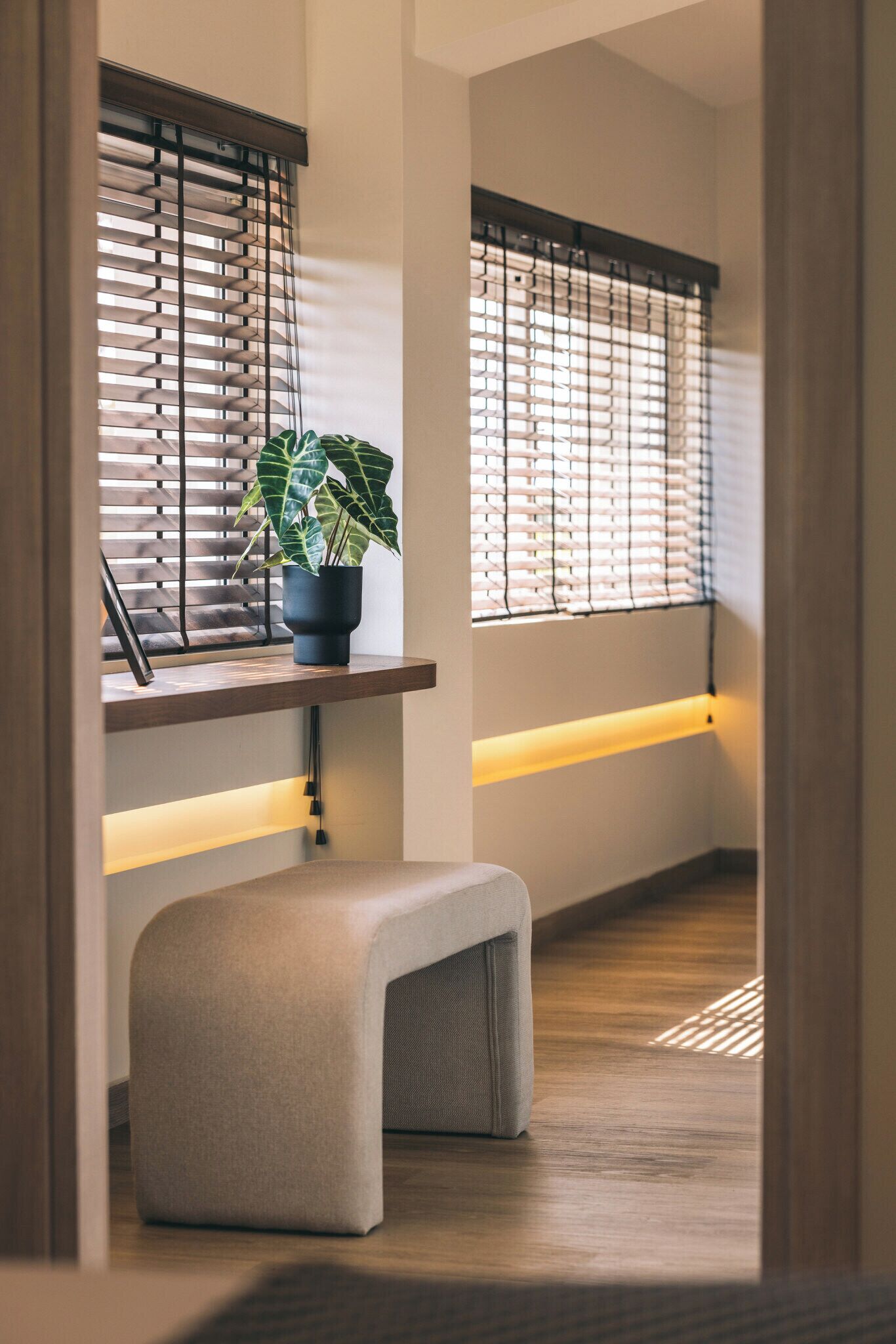 Ein modernes Interieur mit einer Bank, einem Topf mit Pflanze und zwei Fenstern mit Jalousien.