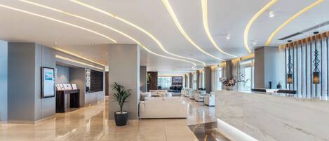 A modern hotel lobby with a marble reception desk, a seating area with sofas, and a large potted plant.
