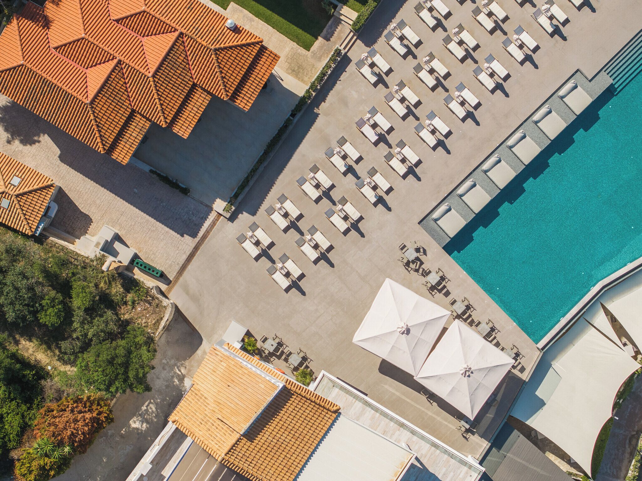 Vista aérea de un hotel con piscina, varias zonas de descanso con sombrillas y una estructura de techo de baldosas.
