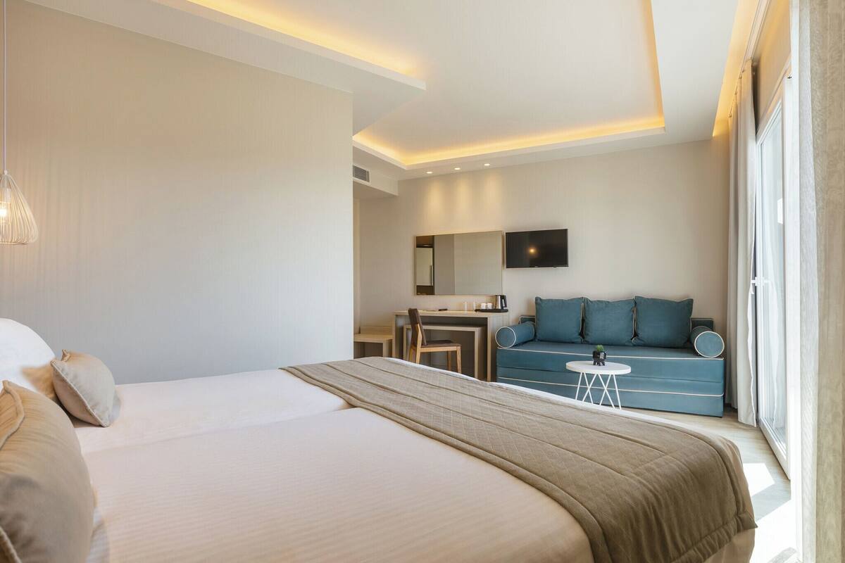 A modern hotel room with a large bed, a desk, a sofa, and a TV.