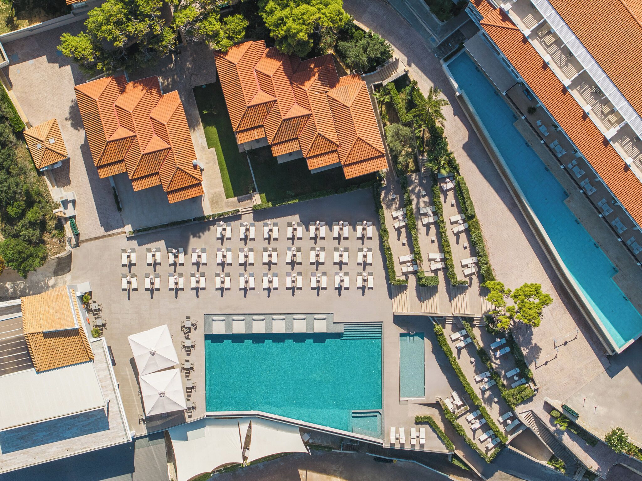 Vista aerea di un resort con una grande piscina, diverse aree relax con lettini e una zona con portico coperto.