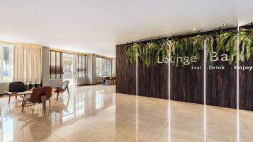 Een moderne loungeruimte met een houten wand en hangplanten, een zithoek met stoelen en een gepolijste vloer.