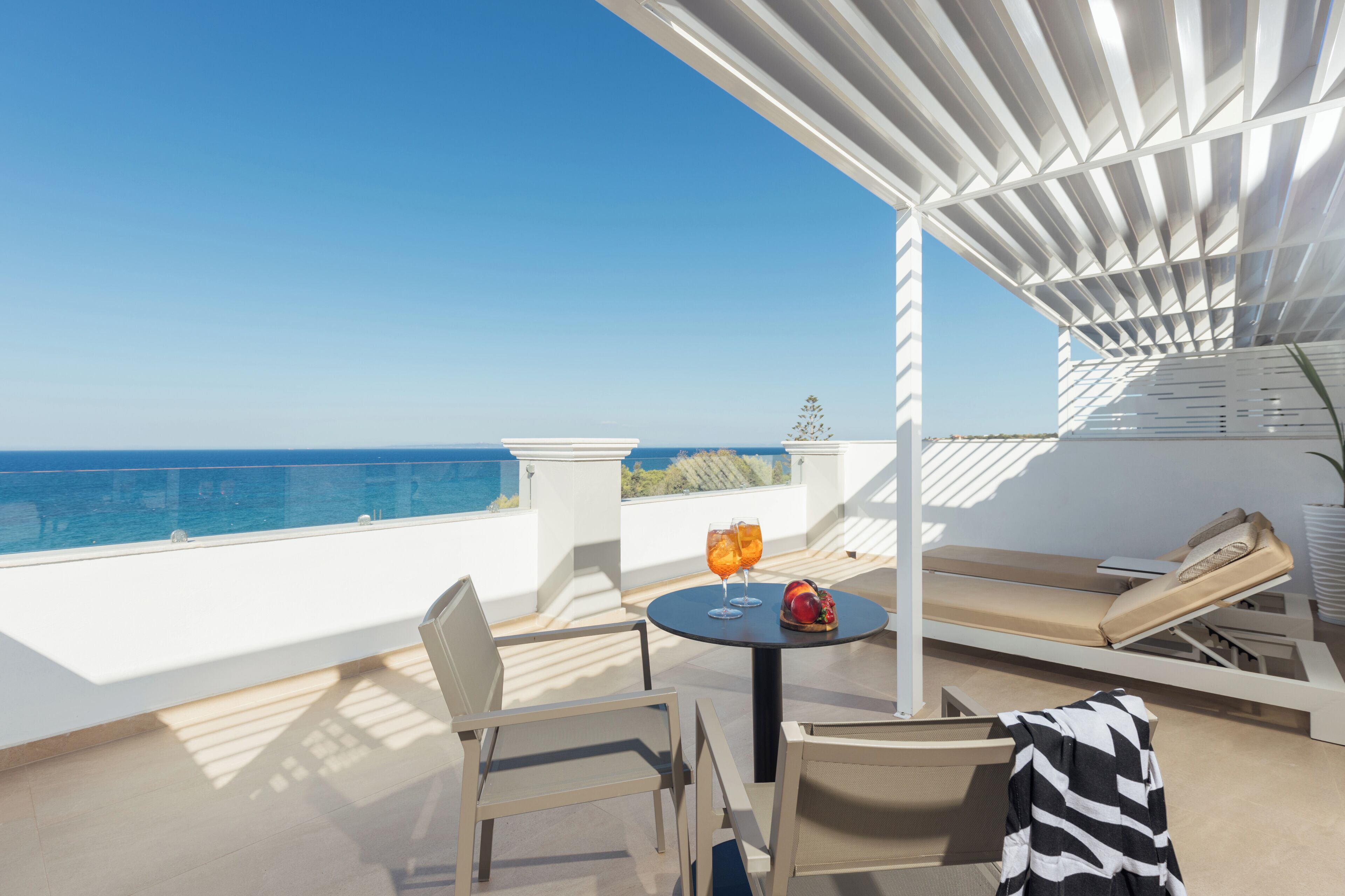 Una terraza con mesa, sillas y un sillón de descanso con vistas al mar.