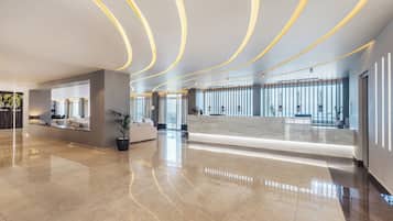 A spacious lobby with a polished marble floor, a reception desk, and a seating area with a sofa and potted plants.