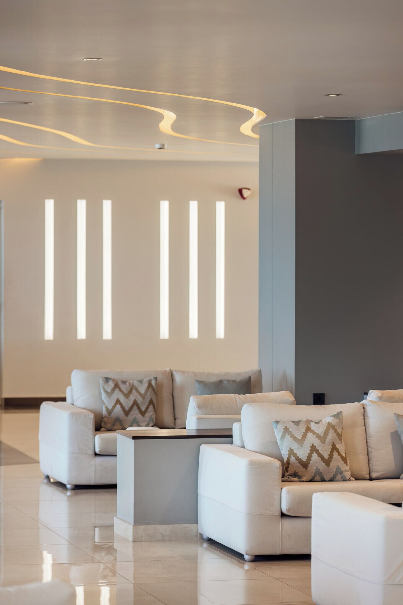 En moderne hotellobby med et siddeområde med hvide sofaer og et centralt kaffe bord.