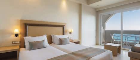 A hotel room with two beds, a balcony with a table and chairs, and a view of the sea.